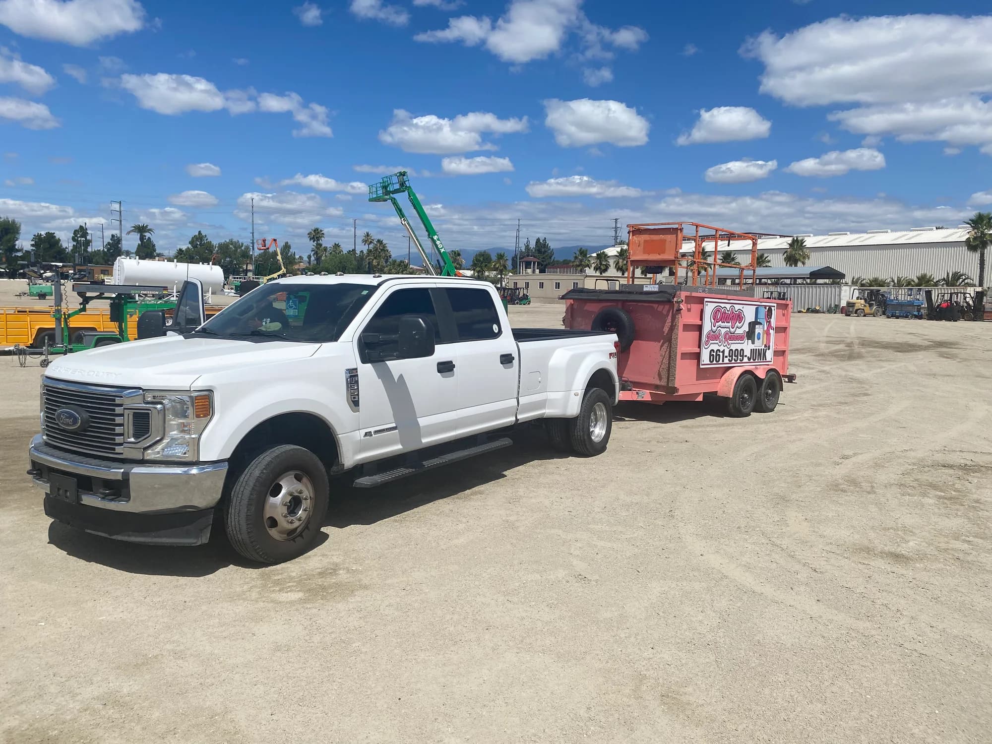 Pinky's white pickup truck attached to the bright pink junk-removal trailer at a commercial equipment yard.