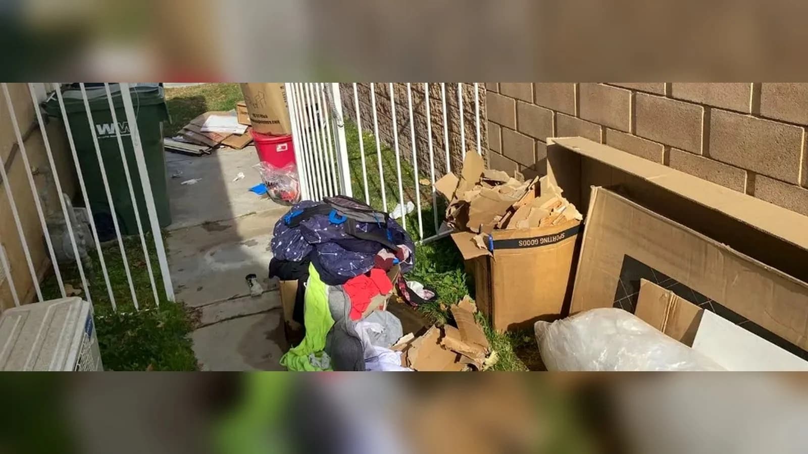 Lancaster side yard before cleanup with bags, boxes, cardboard, and loose household junk along the walkway.