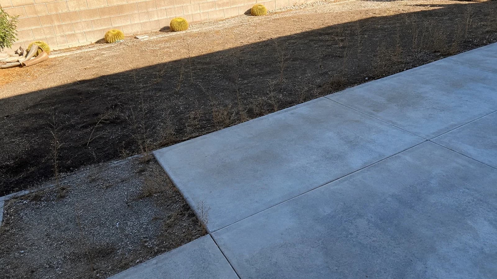 Quartz Hill backyard slab after cleanup with the concrete swept and the dry planter bed untouched.
