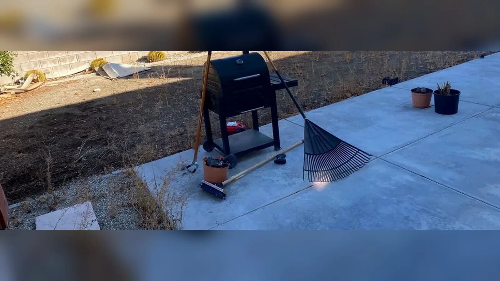 Quartz Hill backyard slab before cleanup with a grill, rake, poles, pots, and scattered small items.