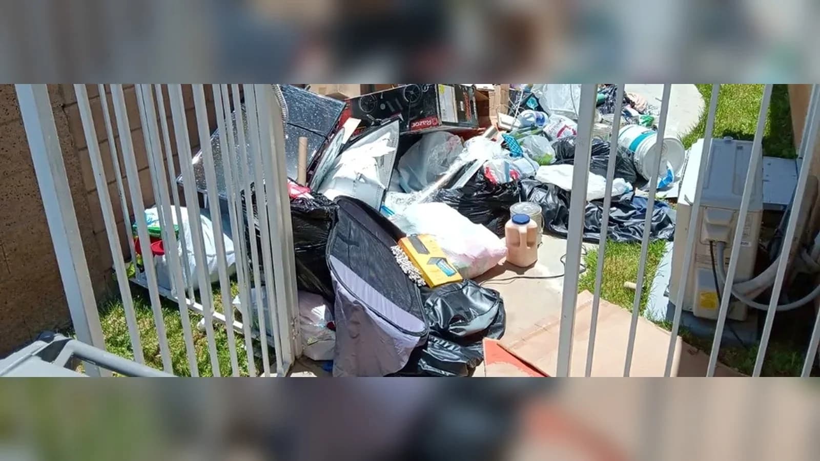 Side-gate walkway filled with bags, cardboard, containers, and household junk before removal.