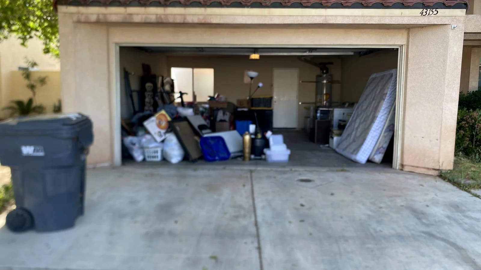 Palmdale garage before cleanup with a mattress, bags, boxes, lamps, and household items at the opening.
